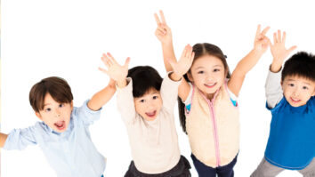 four kids in a row smiling with hands in the air